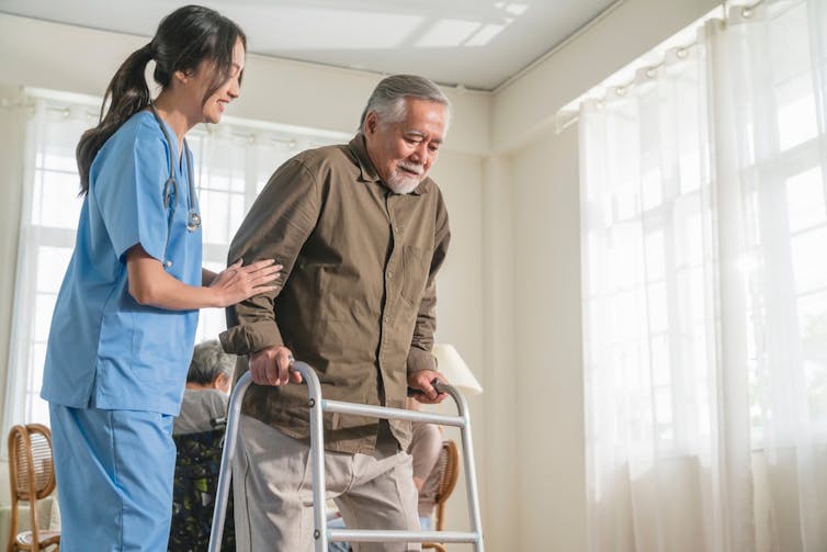 Health worker helping elderly man with walking frame
